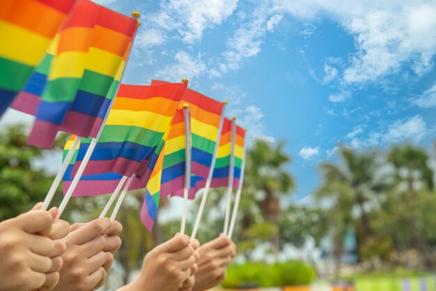 Foto mãos de pessoas da diversidade levantando bandeiras coloridas de arco-íris lgbtq juntas, um símbolo para a comunidade lgbt