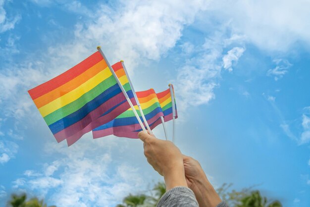Foto mãos de pessoas da diversidade levantando bandeiras coloridas de arco-íris lgbtq juntas, um símbolo para a comunidade lgbt