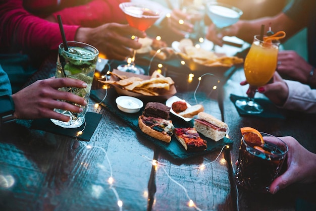 Mãos de pessoas segurando copos de coquetel na mesa de bar