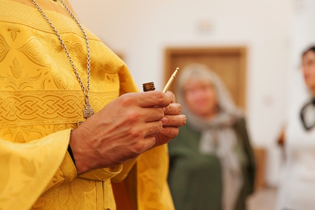 Mãos de sacerdote segurando óleo para unção no batismo no fundo da Igreja Ortodoxa tradicional