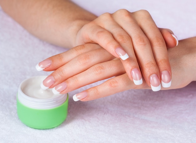 Mãos de spa com manicure francesa perfeita perto do pote de creme