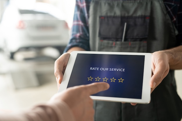 Mãos de trabalhador do centro de manutenção do carro segurando o touchpad com cinco estrelas na tela enquanto o cliente avalia o serviço