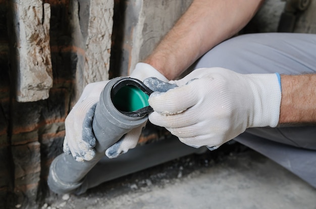 Mãos de trabalhadores estão instalando canos de esgoto na cozinha de um apartamento.