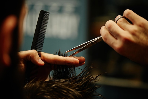 Mãos de um barbeiro, o homem no processo de cortar o cabelo com uma tesoura na barbearia.