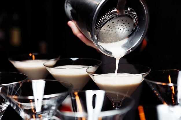 mãos de um barman segurando uma coqueteleira servindo uma bebida em uma taça de martini.