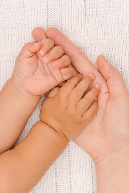 Mãos de um bebê dormindo na palma da mão de uma mãe, sobre um fundo branco. Foto vertical