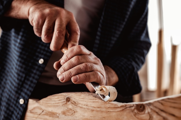 Mãos de um carpinteiro trabalhando com cinzel e martelo