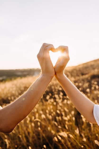 Foto mãos de um casal fazendo uma forma de coração em um campo.