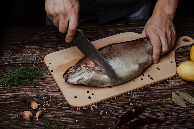 Mãos de um chef masculino, esculpindo truta em uma mesa de madeira na cozinha