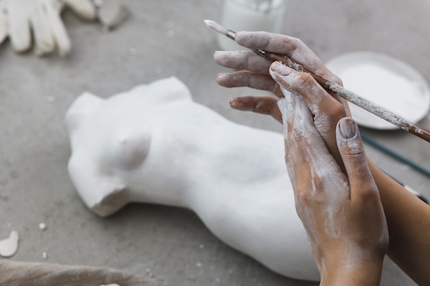 Mãos de um escultor em gesso com um pincel