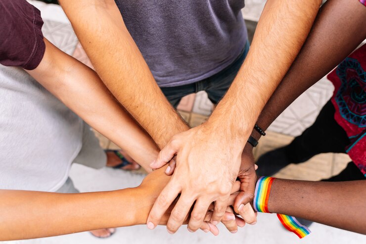 Mãos de um grupo de pessoas de diferentes etnias com uma pulseira de bandeira lgtb