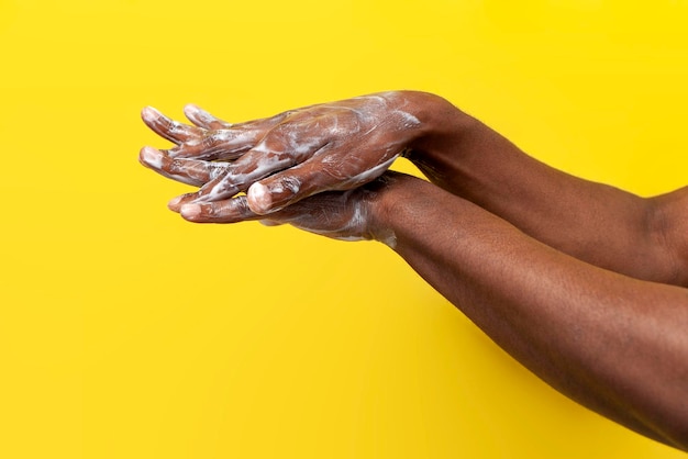 mãos de um homem afro-americano em sabão e espuma em fundo amarelo o cara lava as mãos