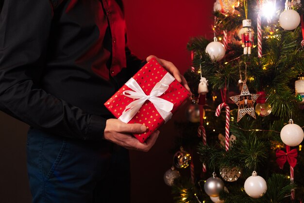 Mãos de um homem com uma caixa de presente na árvore de Natal para comemorar o ano novo