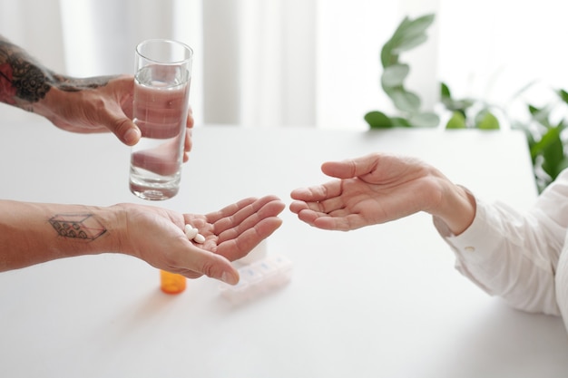 Mãos de um homem dando um copo de água e comprimidos ou suplementos para sua mãe idosa