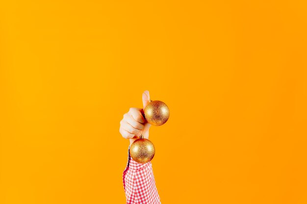 Mãos de um homem em um fundo amarelo, segurando brinquedos de ano novo, bolas de cor dourada