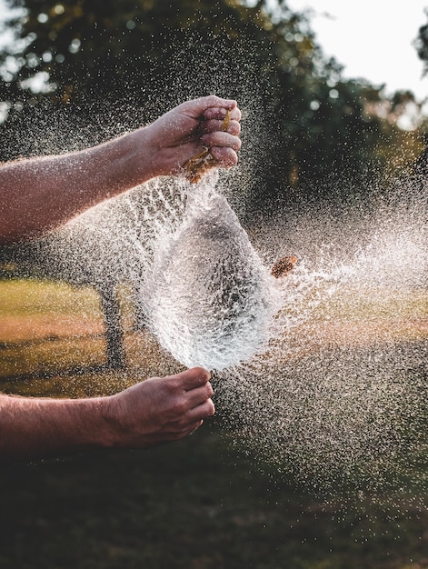 Mãos de um homem explodindo um balão cheio de água no parque