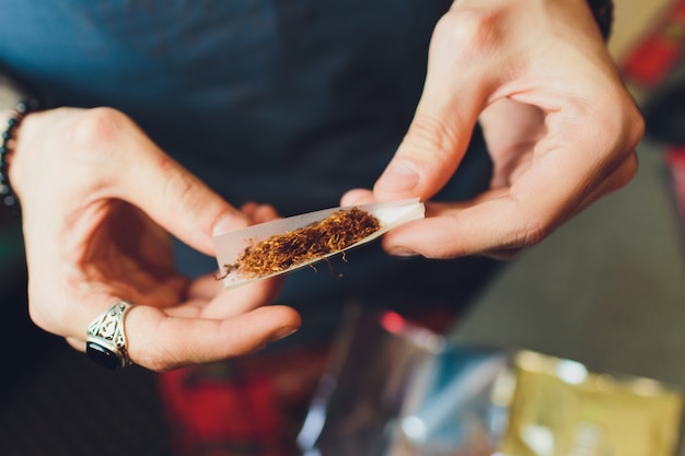 Mãos de um homem rolando um cigarro. O conceito de maconha, drogas, dependência.