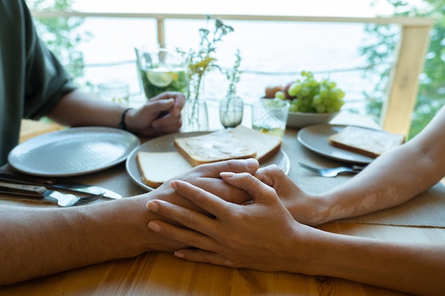 Mãos de um jovem casal carinhoso sentado à mesa servida
