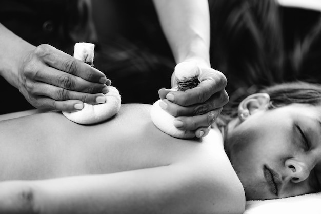 Foto mãos de um massagista ayurvédico pressionando sacos de bolus de ervas na pele dos clientes