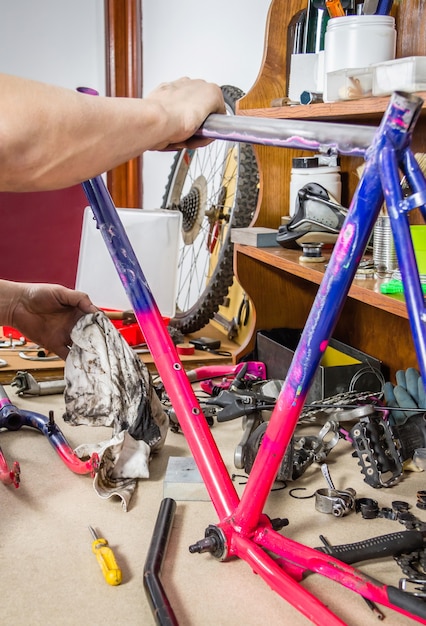 Mãos de um mecânico de bicicletas de verdade limpando uma bicicleta com estrutura danificada em uma oficina