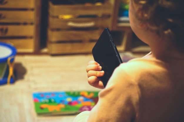 Mãos de um menino brincando com um smartphone em vez de seus brinquedos (brinquedos e livros de fundo)