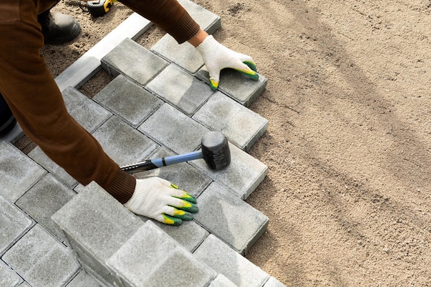Mãos de um trabalhador instalando lajes de pavimentação de blocos de concreto com um martelo de borracha