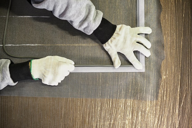 Mãos de um trabalhador na fábrica fazem uma rede mosquiteira para janelas de plástico