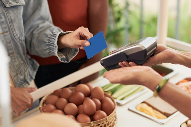 Mãos de uma cliente que paga com cartão de crédito ao comprar produtos no mercado local