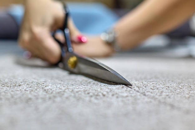 Mãos de uma costureira com manicure rosa cortando tecido com tesoura