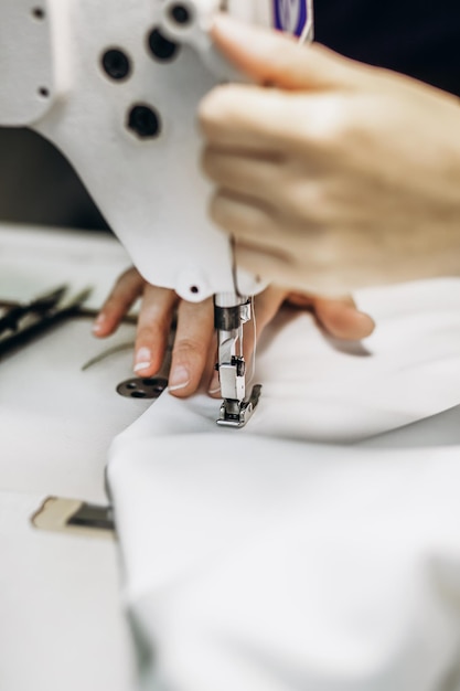 Mãos de uma costureira costurando roupas de tecido branco em uma máquina de costura fechada