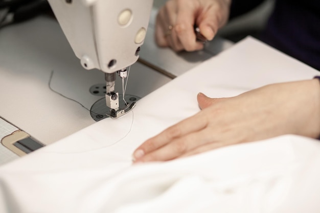 Mãos de uma costureira costurando roupas de tecido branco em uma máquina de costura fechada