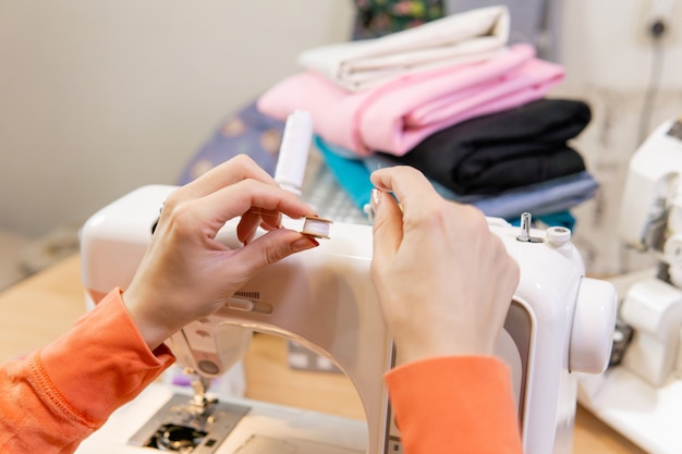 Mãos de uma costureira enrolando linha de um carretel para uma bobina, close-up