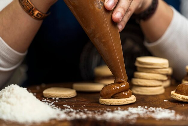 Mãos de uma cozinheira irreconhecível fazendo alfajores argentinos colocando doce de leite em tampas de massa