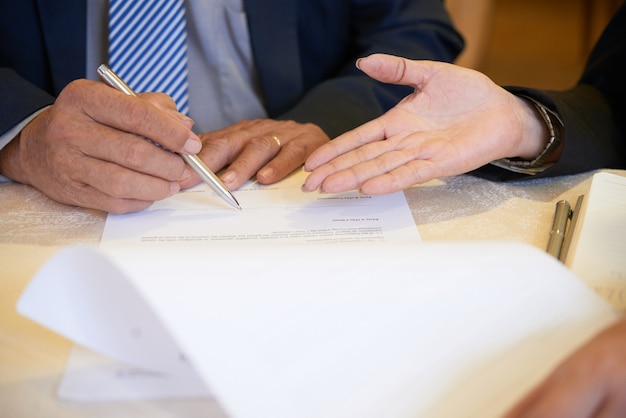 Foto mãos de uma empresária mostrando ao parceiro de negócios onde assinar o contrato