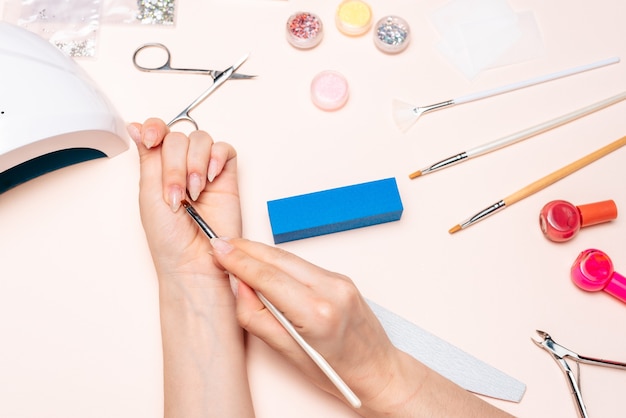 Mãos de uma garota fazendo as unhas, aplicando o gel com um pincel. A vista do topo