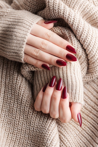 Mãos de uma jovem com manicure vermelho escuro nas unhas