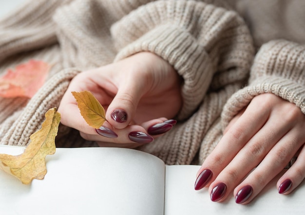 Mãos de uma jovem com manicure vermelho escuro nas unhas