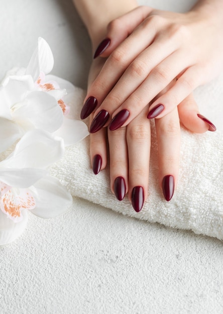 Foto mãos de uma jovem com manicure vermelho escuro nas unhas