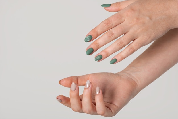 Mãos de uma jovem com unhas verde-oliva fosco e unhas bege brilhantes sobre um fundo cinza claro. unhas de cores diferentes. manicure, salão de beleza. copie o espaço para texto ou logotipo. abstrato