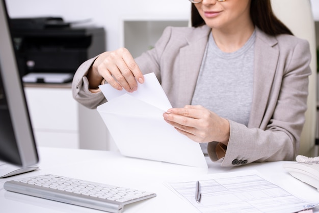 Mãos de uma jovem empresária ou banqueiro colocando papel dobrado em um envelope branco antes de enviar o documento para um dos clientes