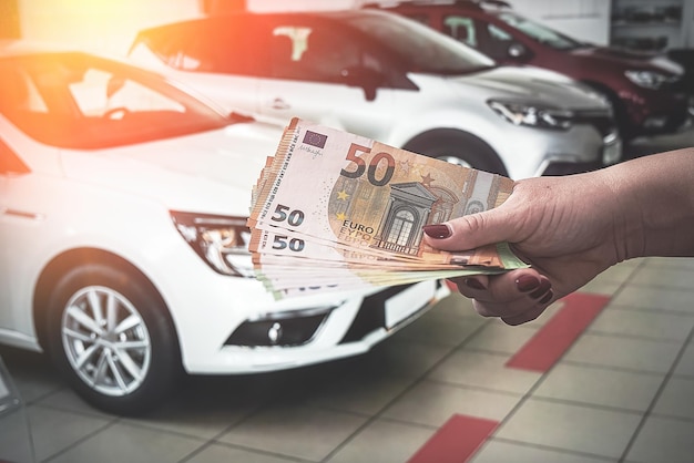 mãos de uma jovem segurando uma nota de euro em um fundo de carros. Conceito de riqueza. Conceito de compra de carro