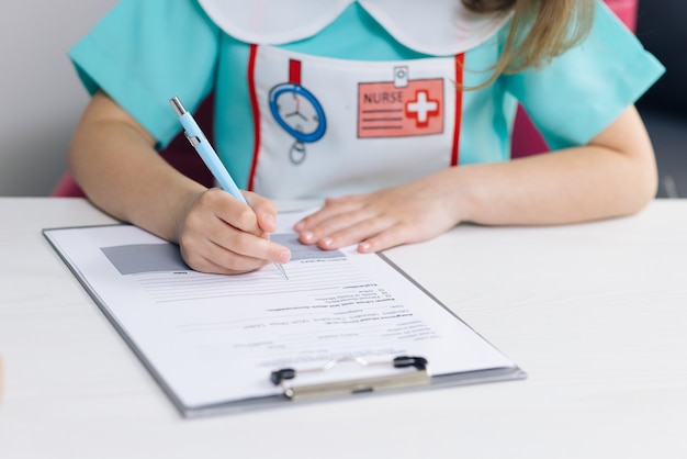 Mãos de uma linda garotinha com o bloco de notas sentado à mesa de madeira e escrevendo notas