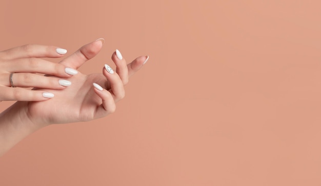 Mãos de uma linda mulher bem cuidada com unhas femininas em um fundo bege Manicure