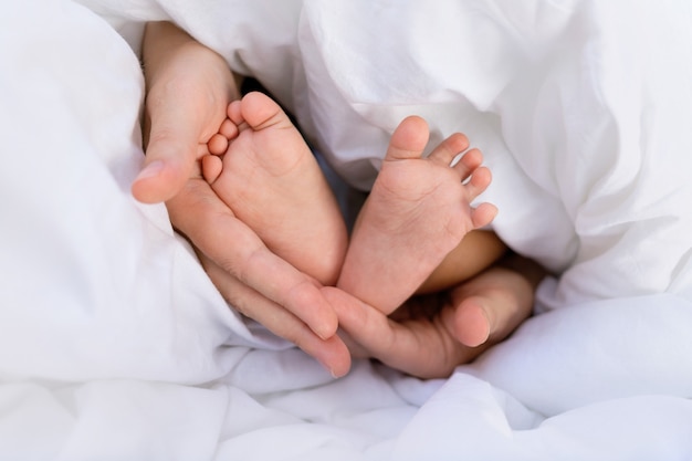 Mãos de uma mãe caucasiana, segurando as pequenas pernas de seu bebê bebê africano negro.