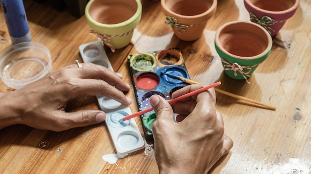 Mãos de uma mulata latina pintando vasos de barro para plantar plantas suculentas