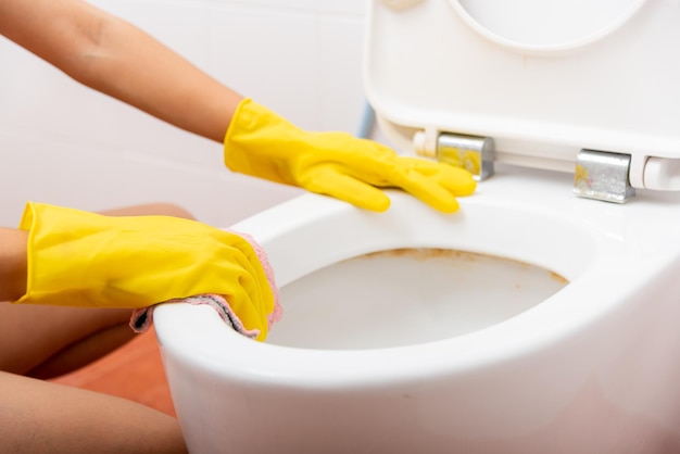 Mãos de uma mulher asiática limpando o assento do vaso sanitário pelo banheiro de pano rosa em casa