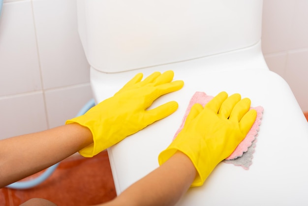 Mãos de uma mulher asiática limpando o assento do vaso sanitário pelo banheiro de pano rosa em casa