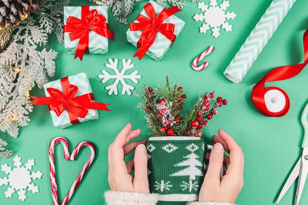 Mãos de uma mulher caucasiana seguram uma caneca em um suéter de natal de malha com ramos de abeto três presentes b