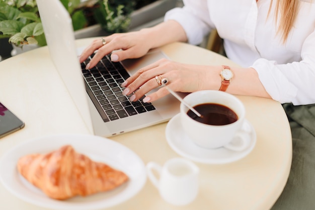 Mãos de uma mulher com café e laptop em um café ao ar livre no verão