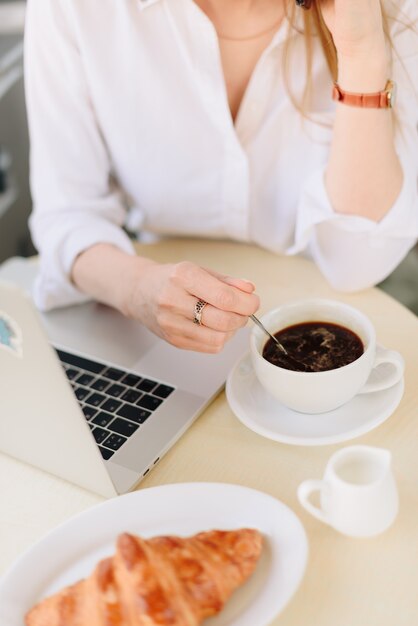 Mãos de uma mulher com café e laptop em um café ao ar livre no verão